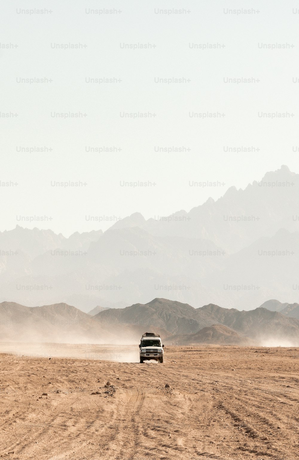 a truck driving through a desert with mountains in the background