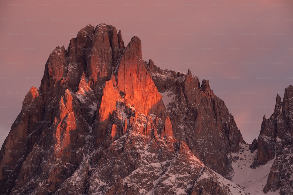 a very tall mountain covered in snow under a pink sky
