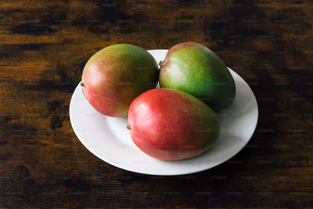 a white plate topped with three apples on top of a wooden table