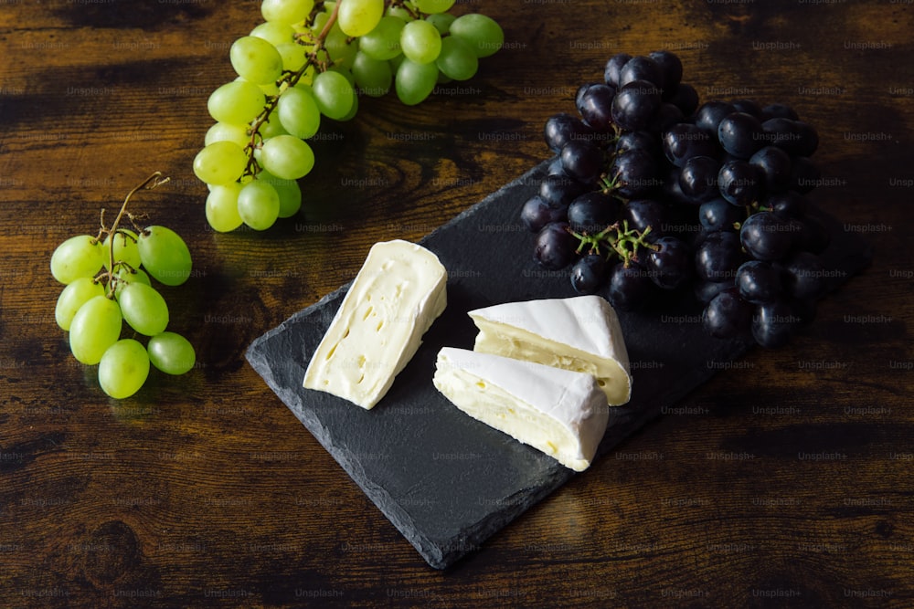 grapes and cheese are on a black plate