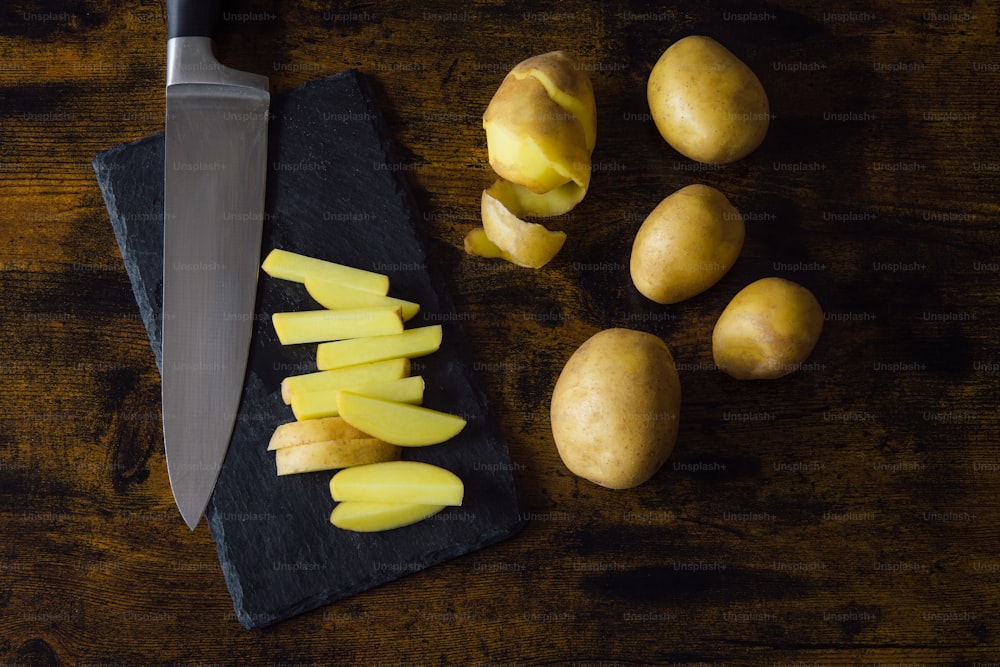 ein Messer und ein paar Kartoffeln auf einem Schneidebrett