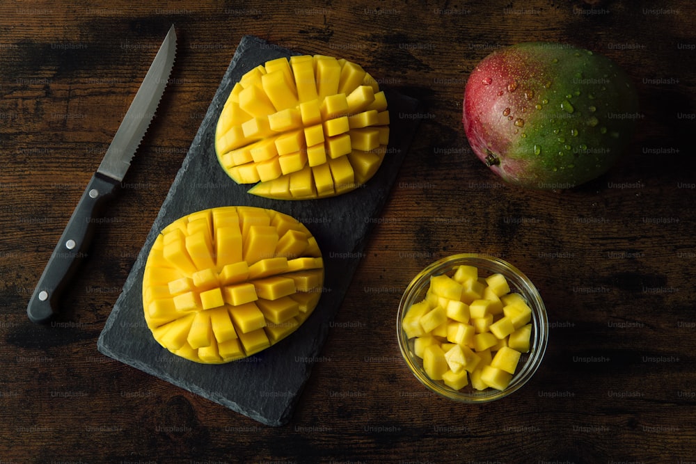 una tabla de cortar cubierta con mangos en rodajas junto a un cuchillo