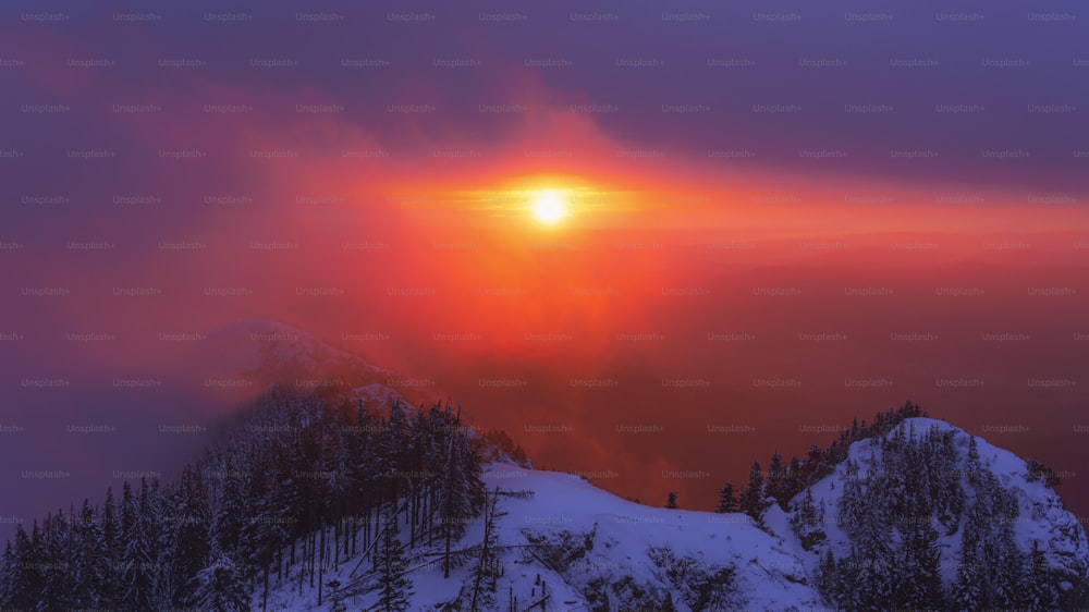 the sun is setting over a snowy mountain