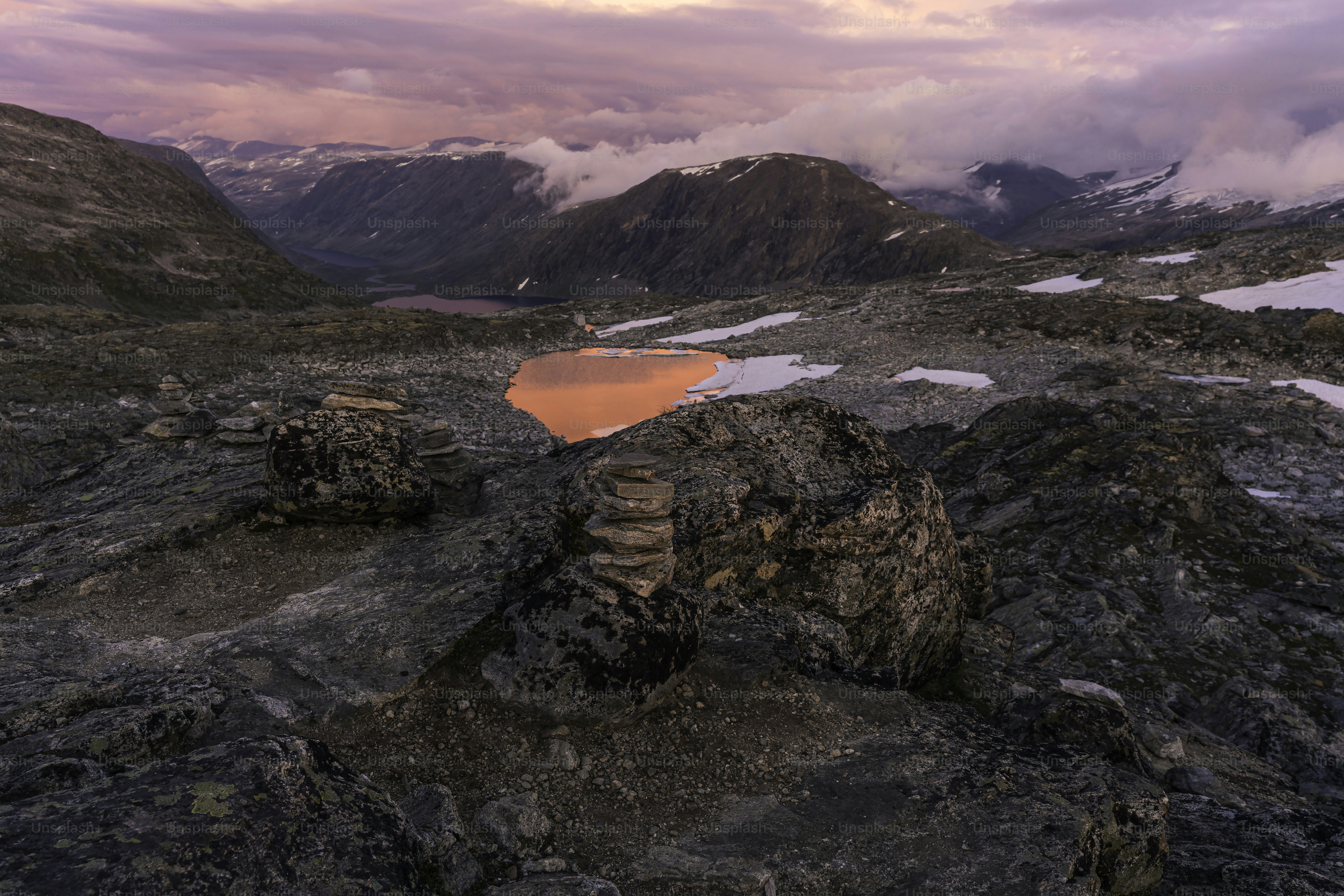 A lake surrounded by rocks under a cloudy sky photo – Wallpaper Image ...