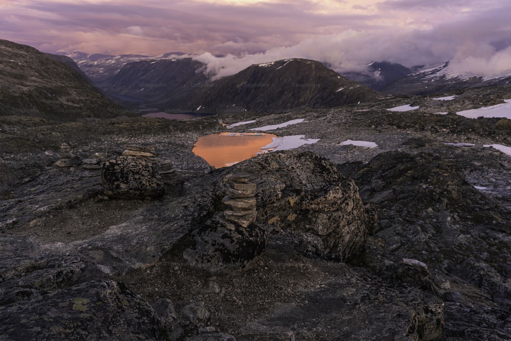 a red lake surrounded by mountains under a cloudy sky