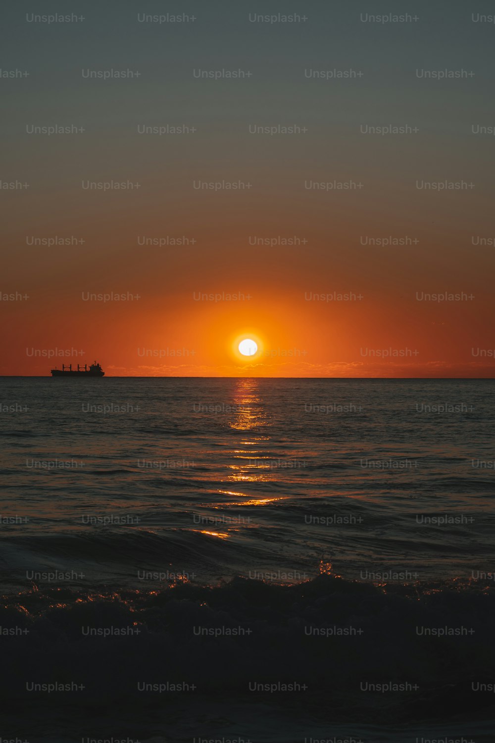 the sun is setting over the ocean with a boat in the distance