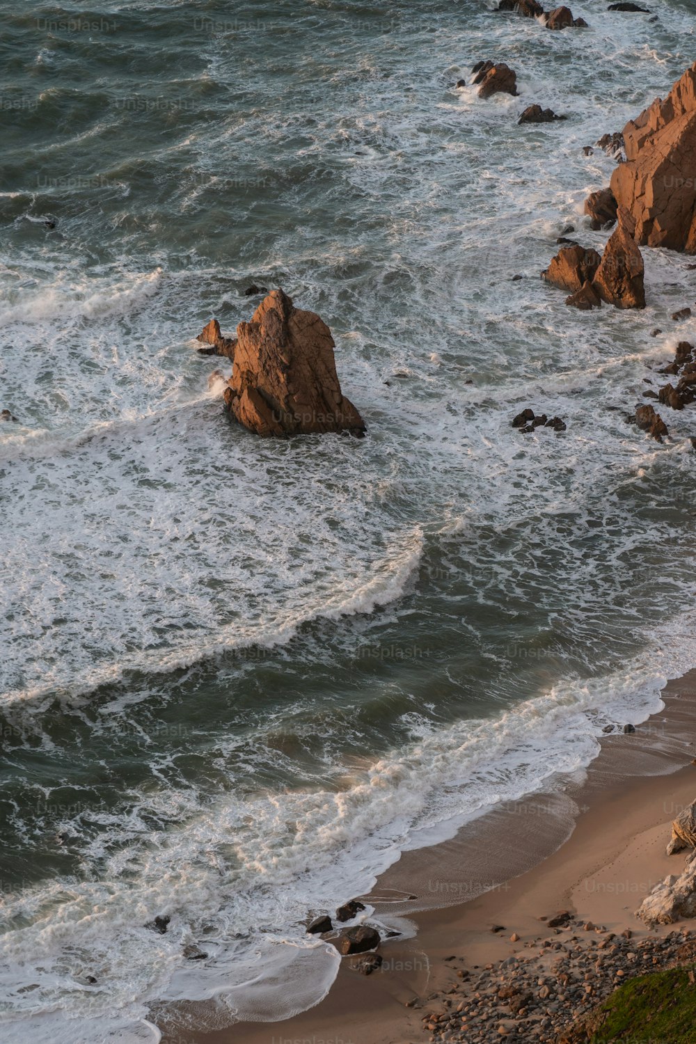 ein paar große Felsen sitzen oben auf einem Strand