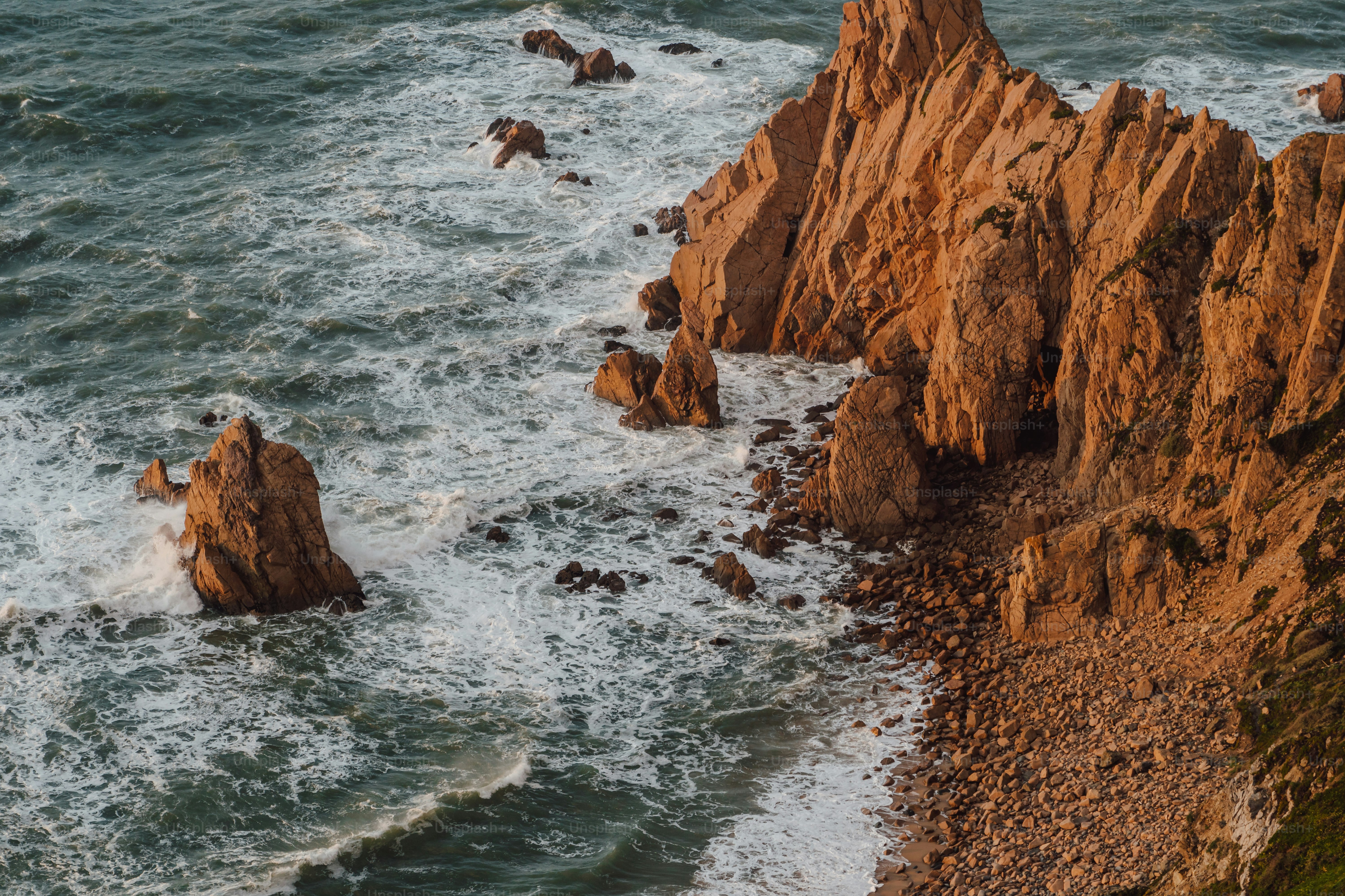 an aerial view of the ocean with rocks in the foreground