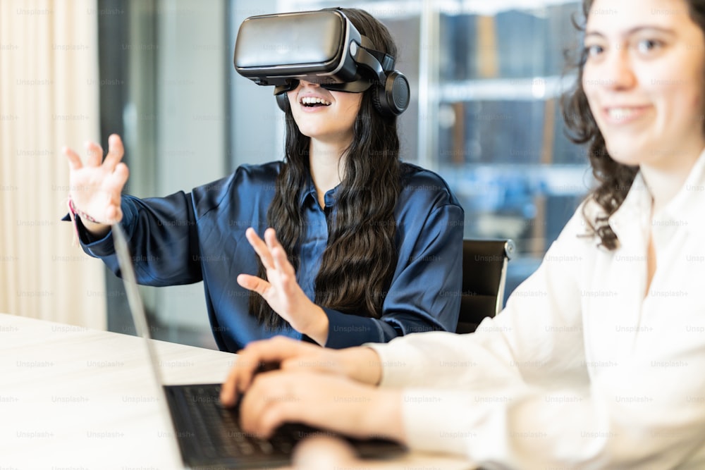 Zwei Frauen sitzen an einem Tisch mit einem Laptop und tragen virtuelle Headsets