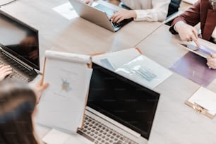 a group of people sitting around a table with laptops