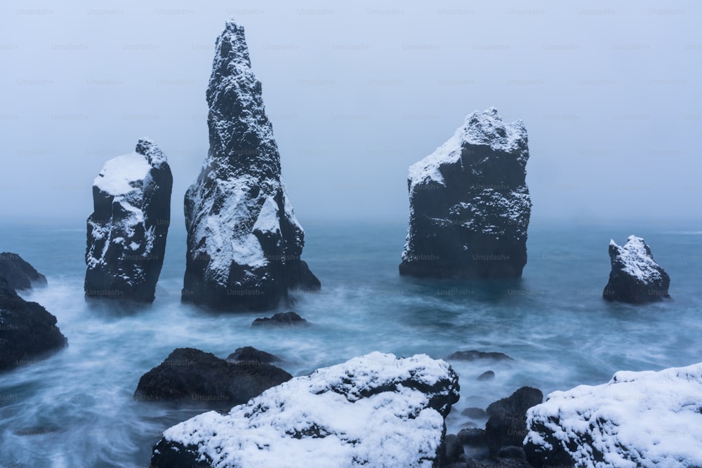 a group of rocks in the water covered in snow