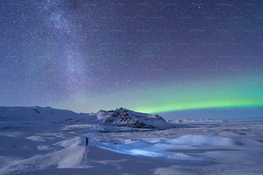uma pessoa em pé no topo de uma encosta coberta de neve sob um céu cheio de estrelas