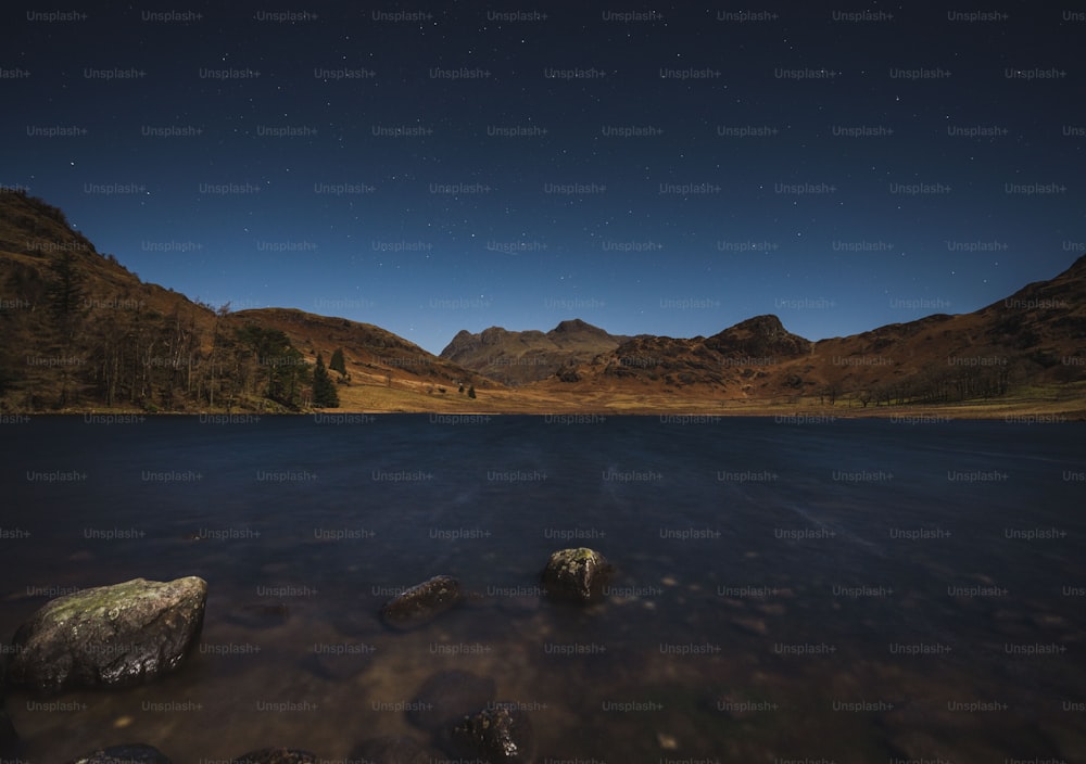 the night sky over a mountain lake with rocks in the foreground