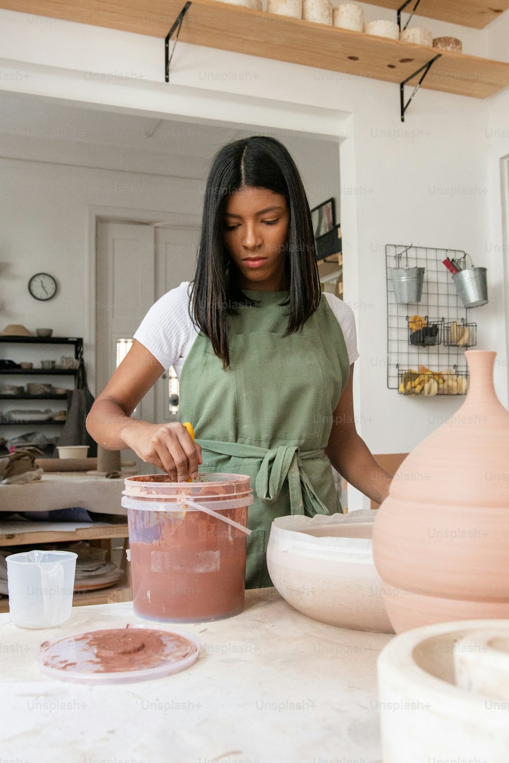 a woman in a green apron is making clay