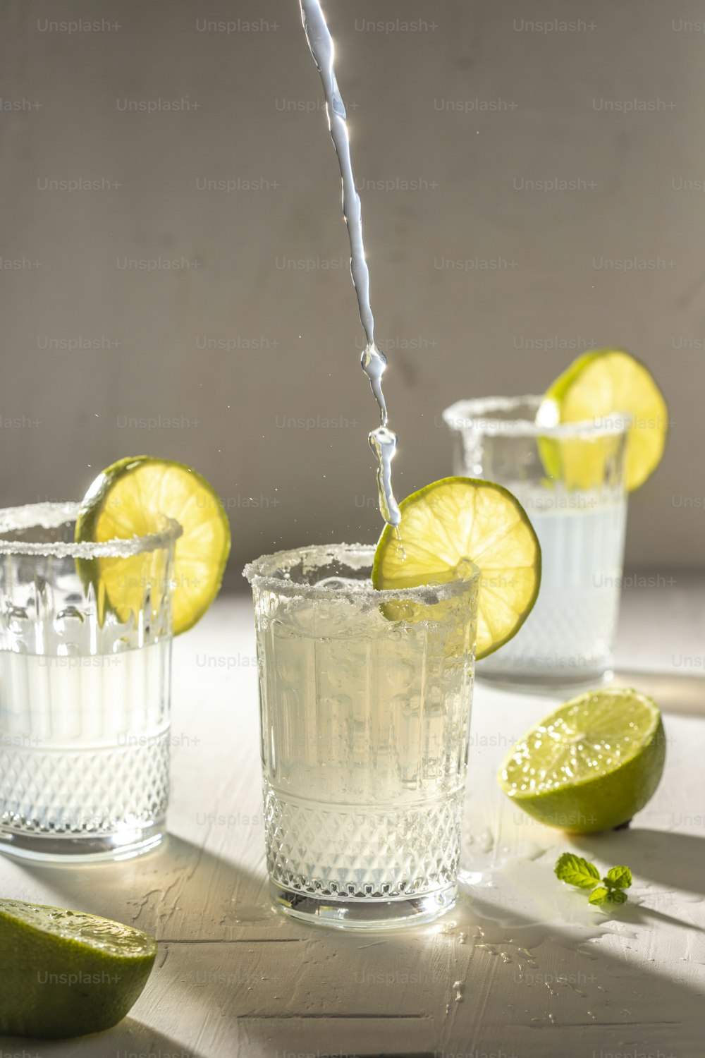 a pitcher of water pouring into a glass filled with ice and limes