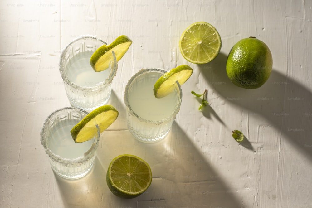 three glasses of water with limes on a table