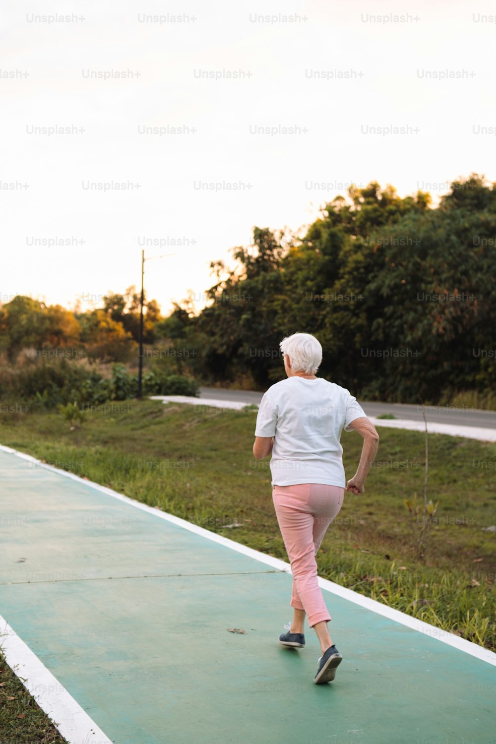 분홍색 바지와 흰색 티셔츠를 입은 여자가 녹색 위를 달리고 있다