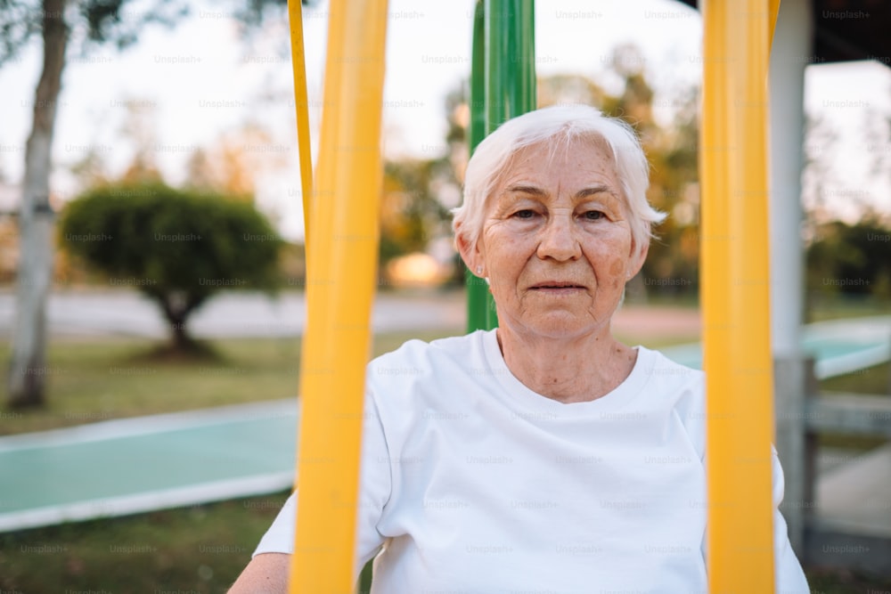 an older woman sitting on a swing in a park