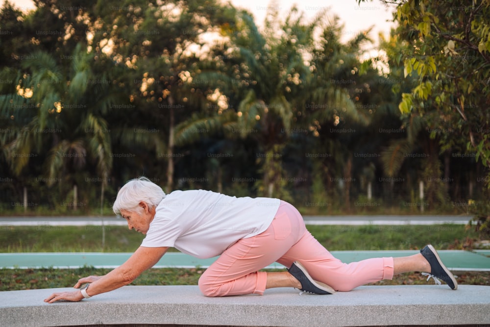 an older woman is stretching on a concrete bench