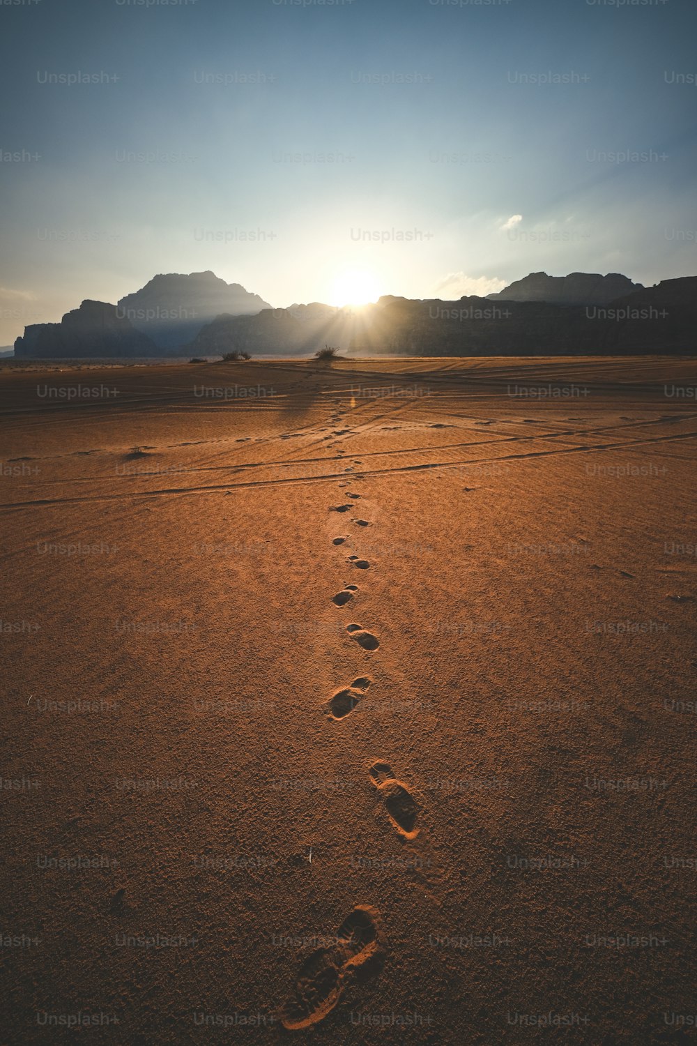 a trail of footprints in the desert at sunset