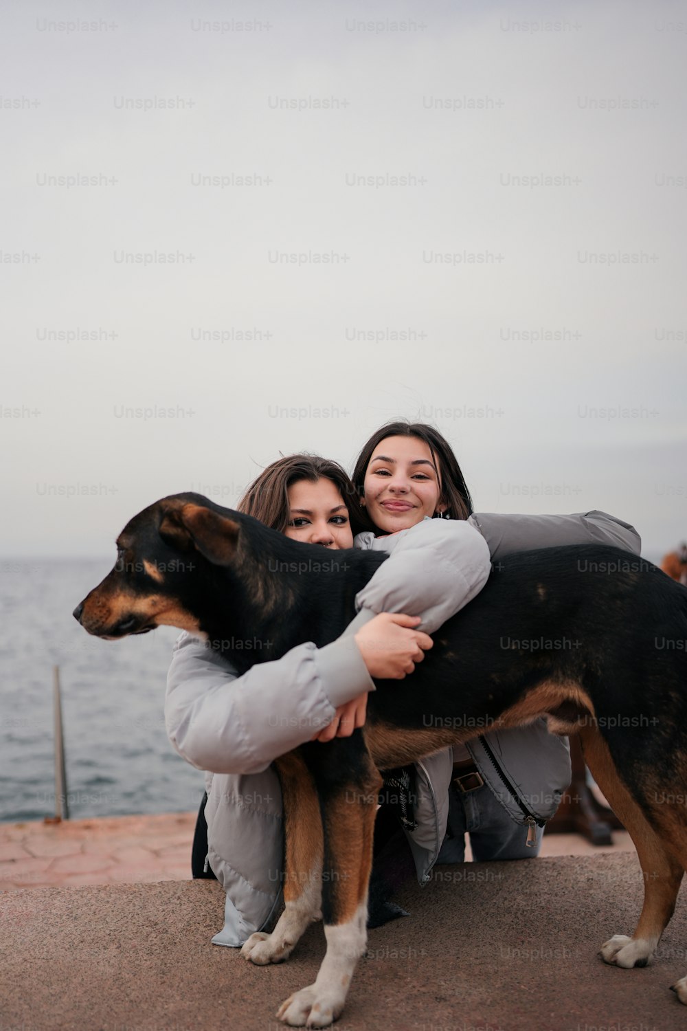 two women hugging a dog on a pier
