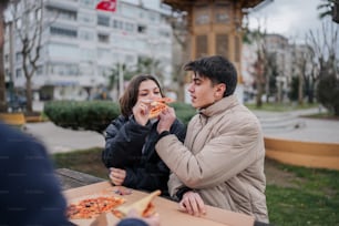 a man and a woman eating pizza on a park bench