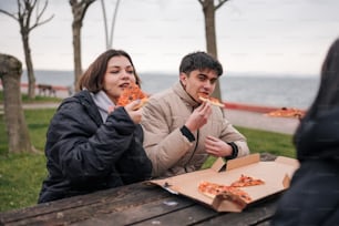 a man and a woman sitting at a picnic table eating pizza