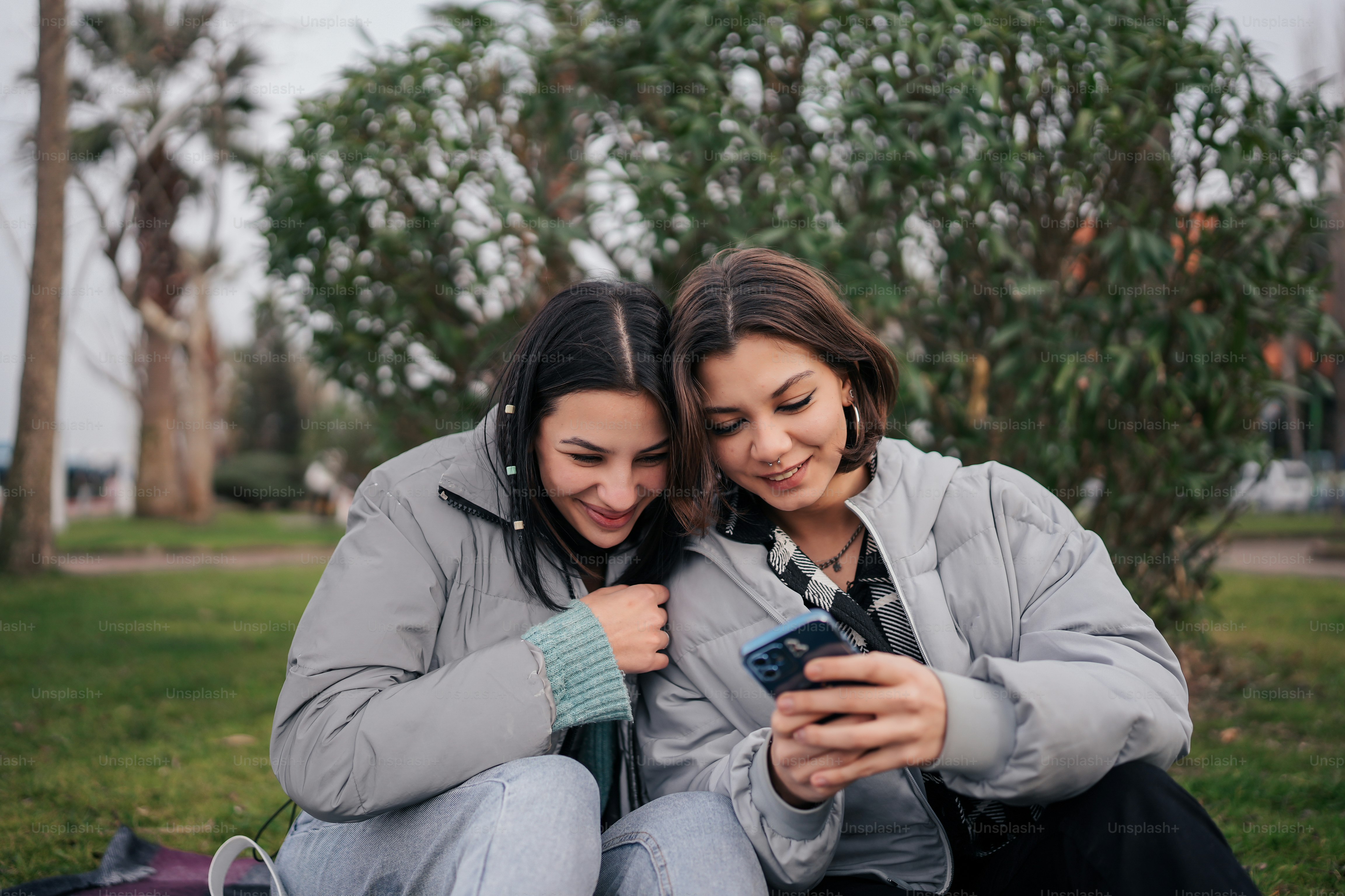 two women sitting on the ground looking at a cell phone