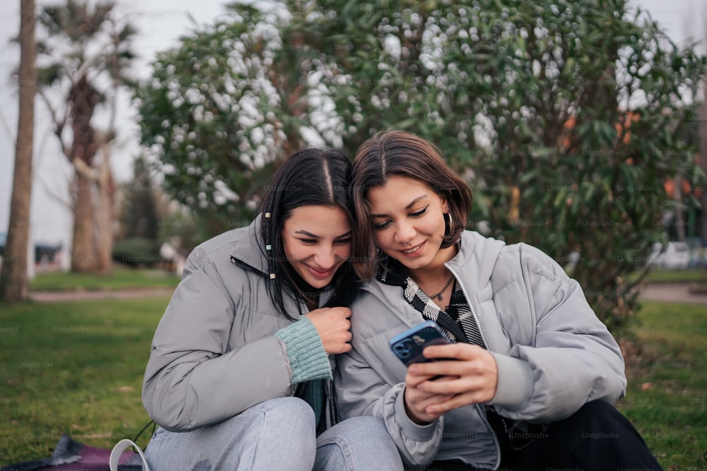 two women sitting on the ground looking at a cell phone