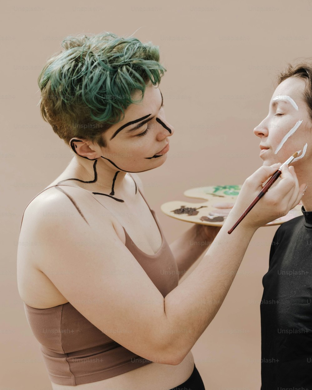 Une femme aux cheveux verts peint le visage d’une autre femme
