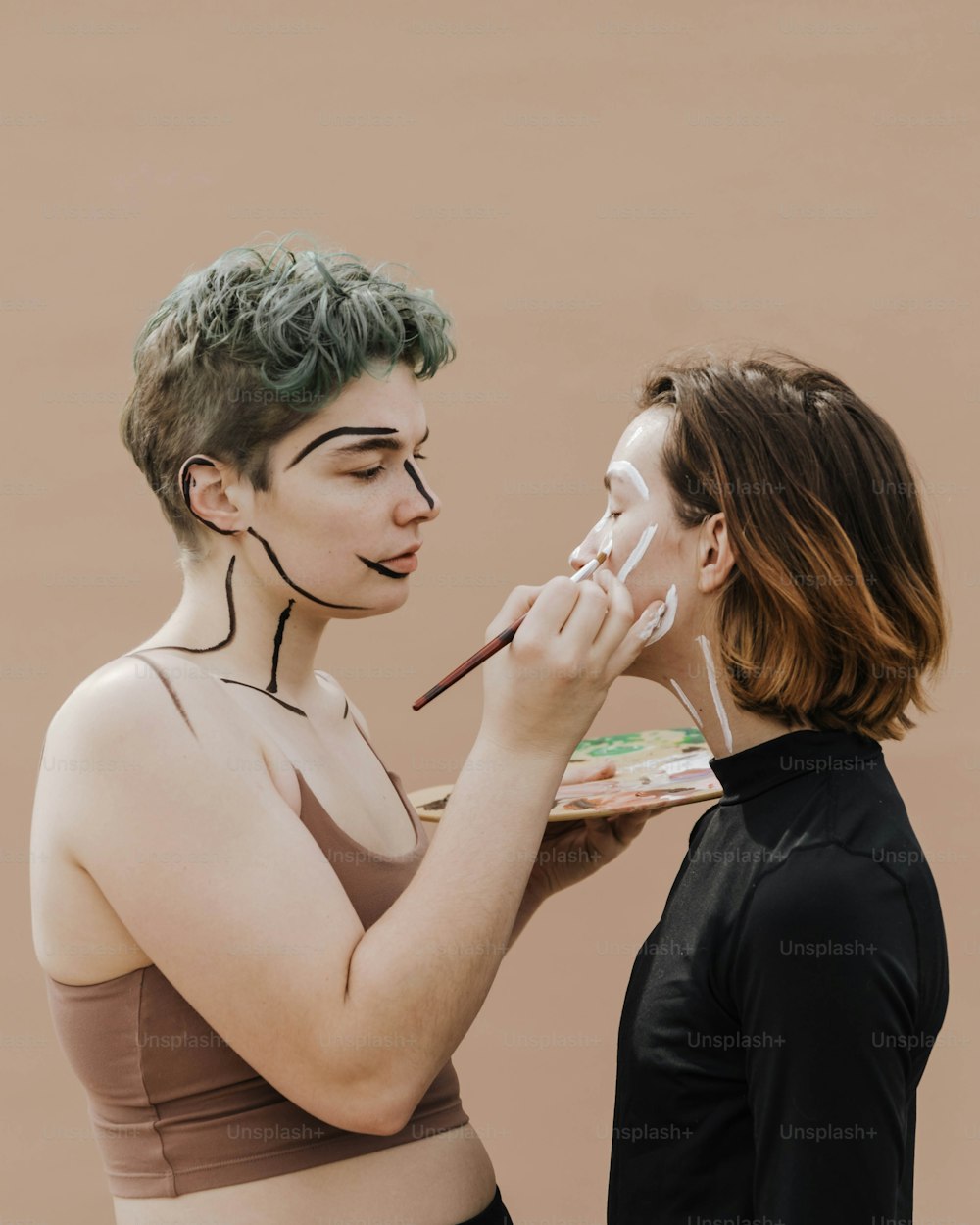 Una mujer está pintando la cara de otra mujer con pintura blanca
