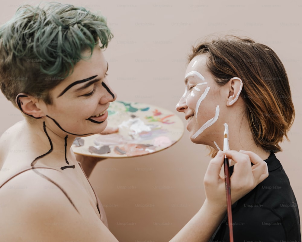 a woman is painting another woman's face with white paint