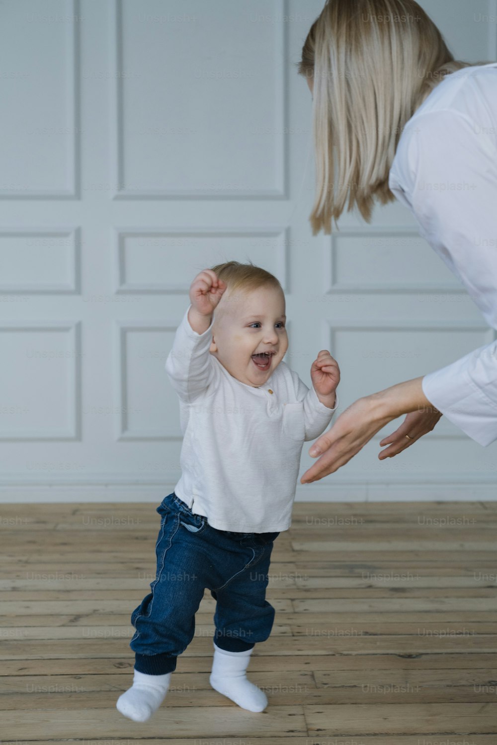 a woman holding a baby's hand while standing on top of a wooden floor