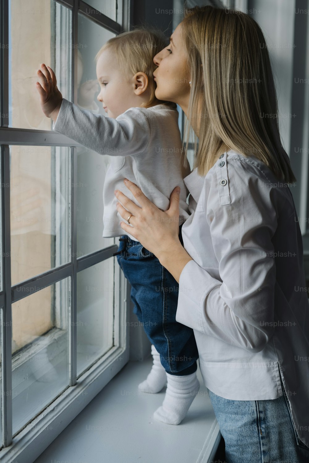 a woman holding a baby looking out of a window