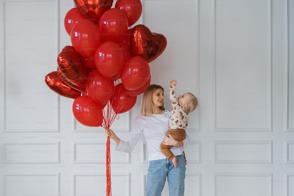 Una mujer sosteniendo a un bebé y un montón de globos rojos