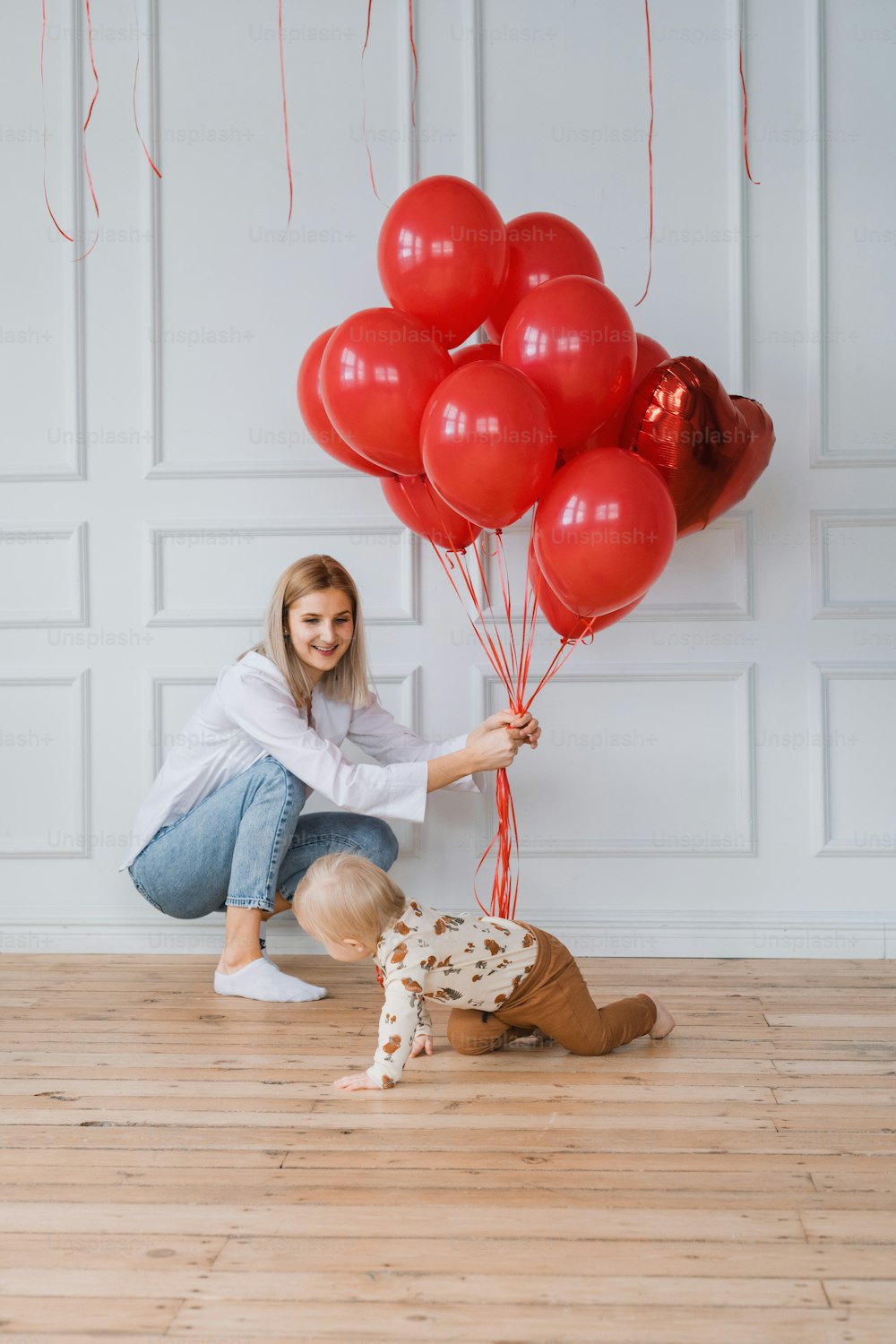a woman kneeling down next to a dog holding a bunch of red balloons