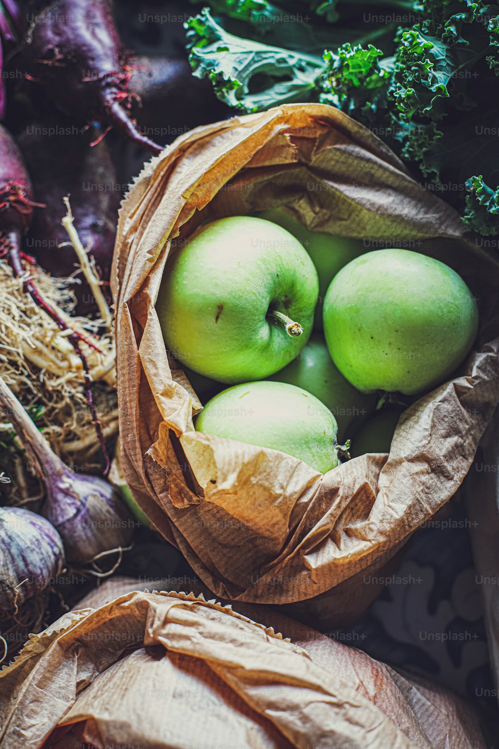 um saco cheio de maçãs verdes sentado em cima de uma pilha de legumes
