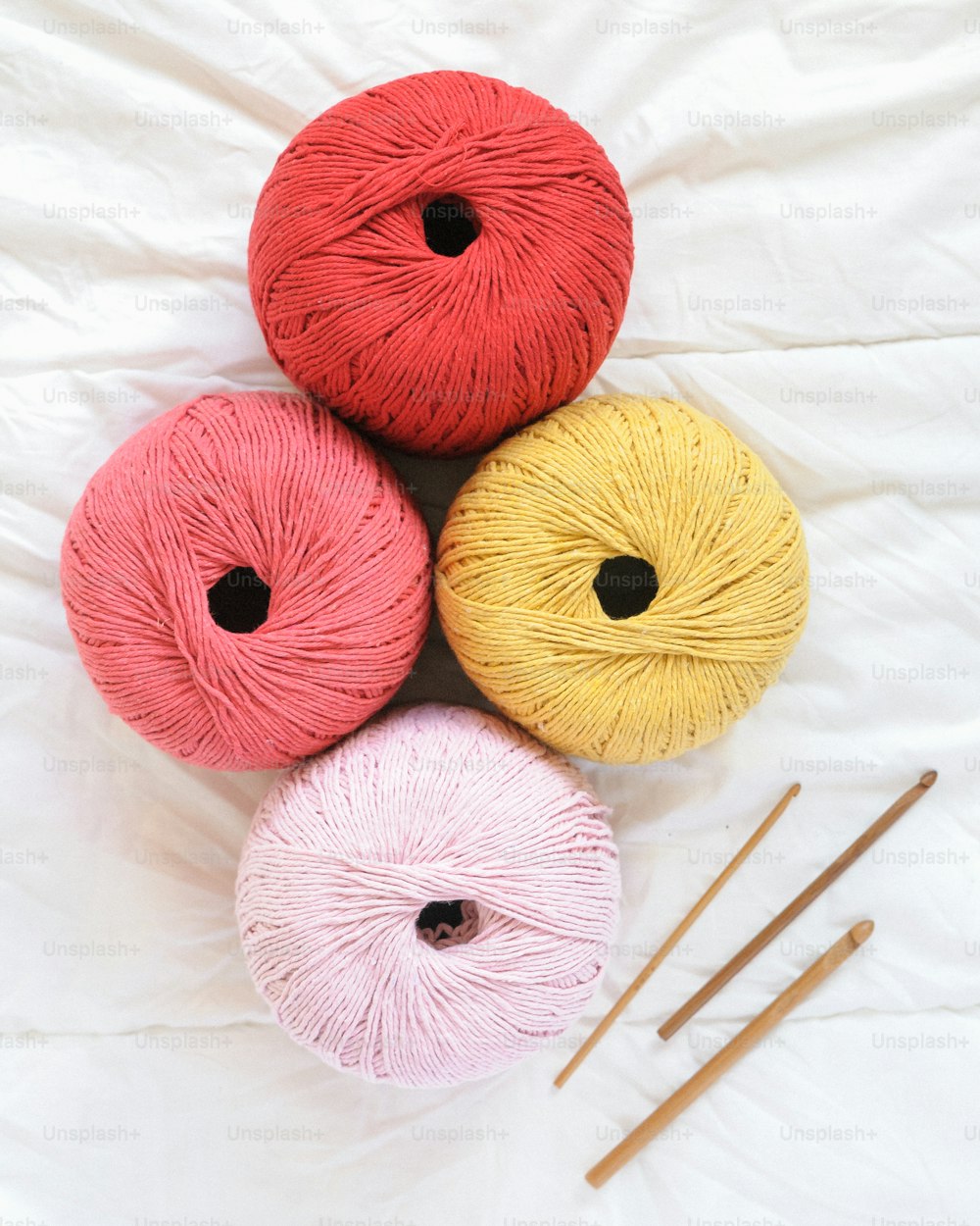 three balls of yarn and knitting needles on a white sheet
