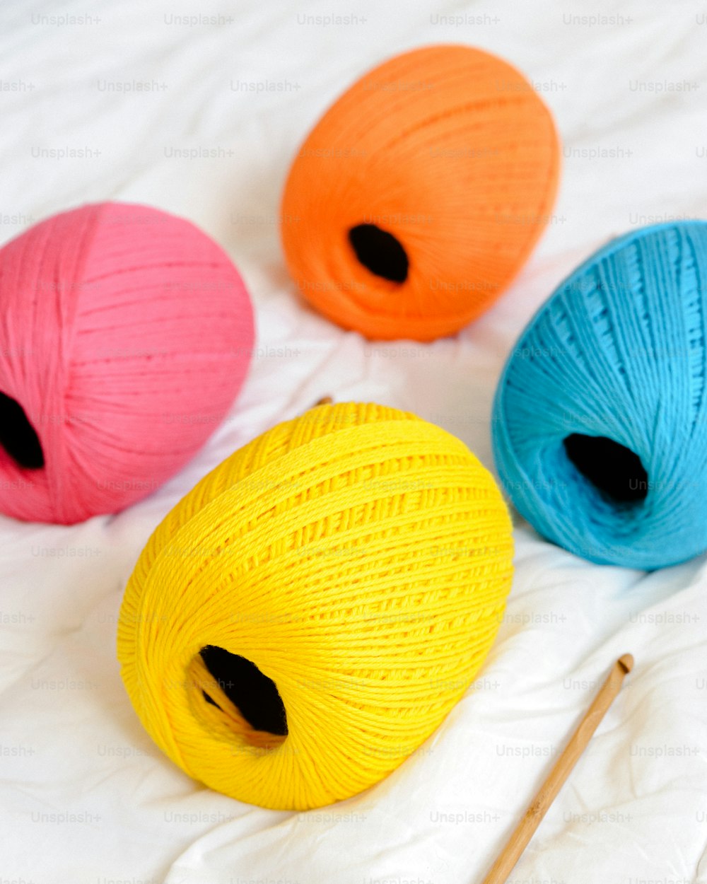 three balls of yarn and a knitting needle on a bed
