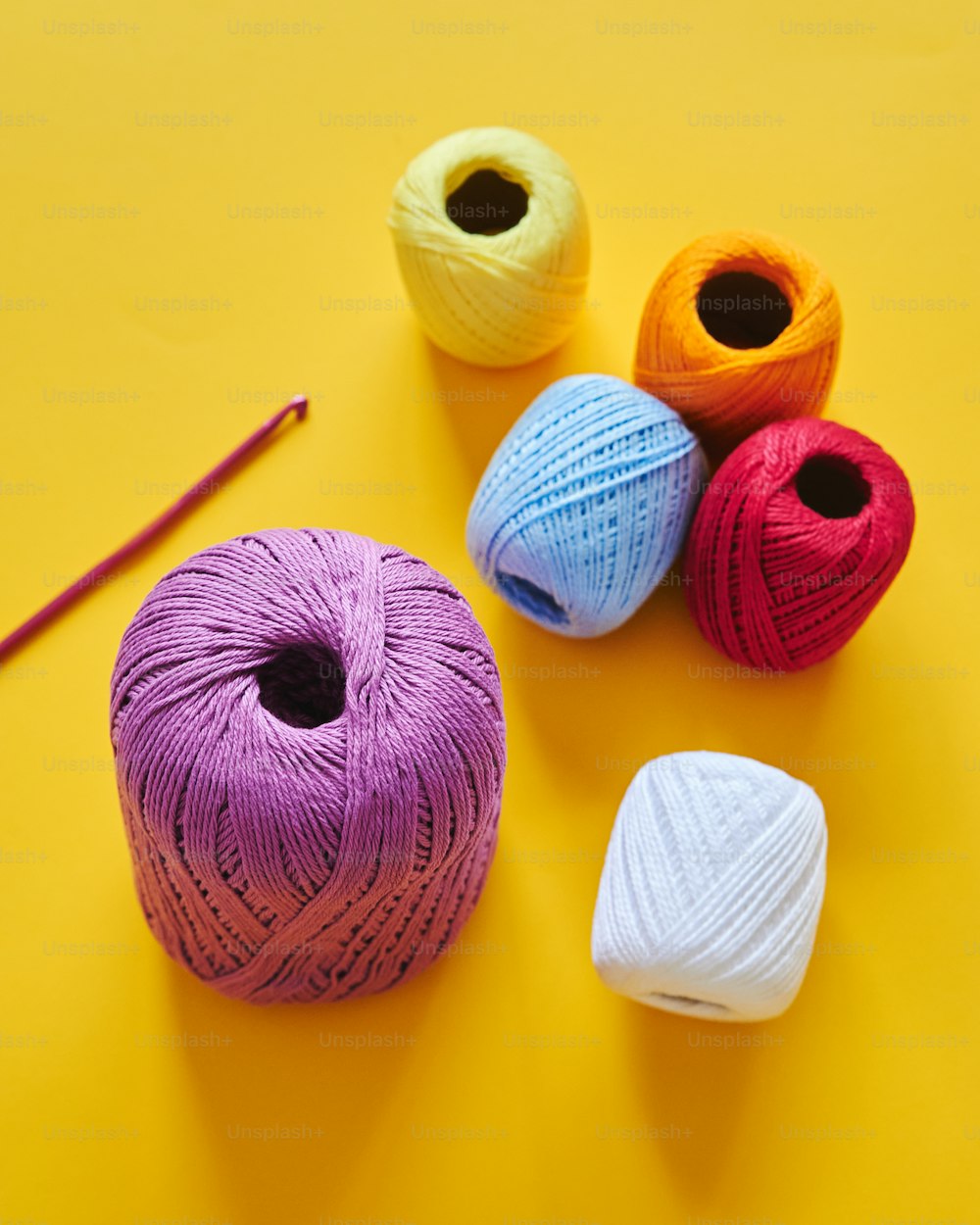 黄色の背景に3つの糸のボールとかぎ針編みのフック