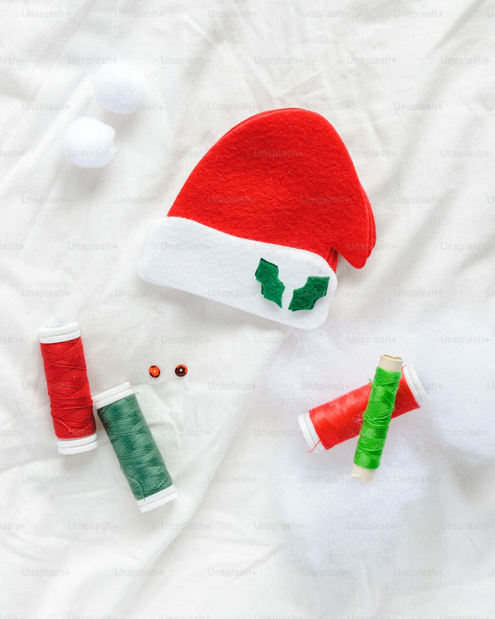 a white sheet with a red and green hat and spools of thread