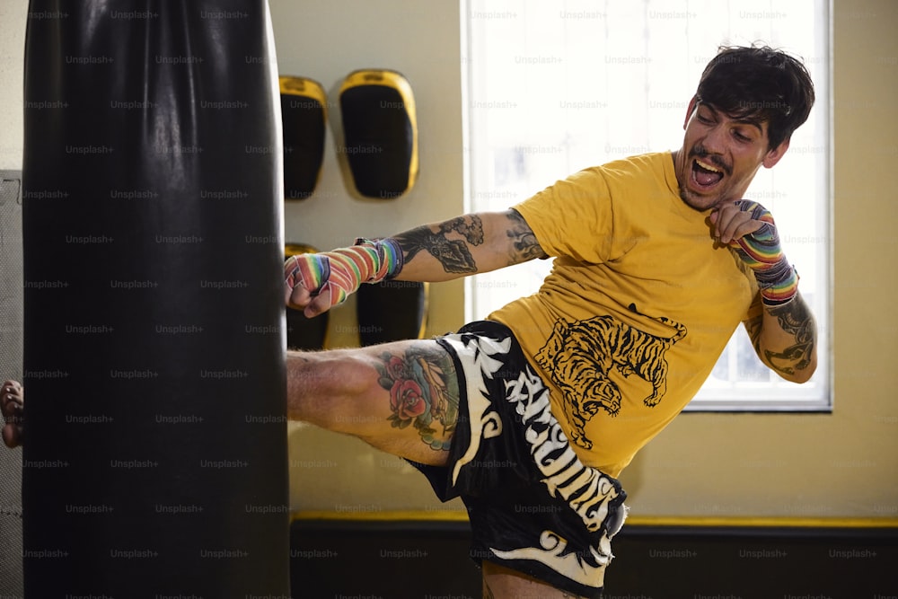 Un homme en chemise jaune donne un coup de pied dans un sac de boxe