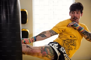 Un hombre con tatuajes en sus brazos y piernas pateando un saco de boxeo
