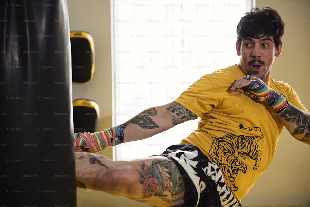 Un uomo con tatuaggi sulle braccia e sulle gambe che prende a calci un sacco da boxe