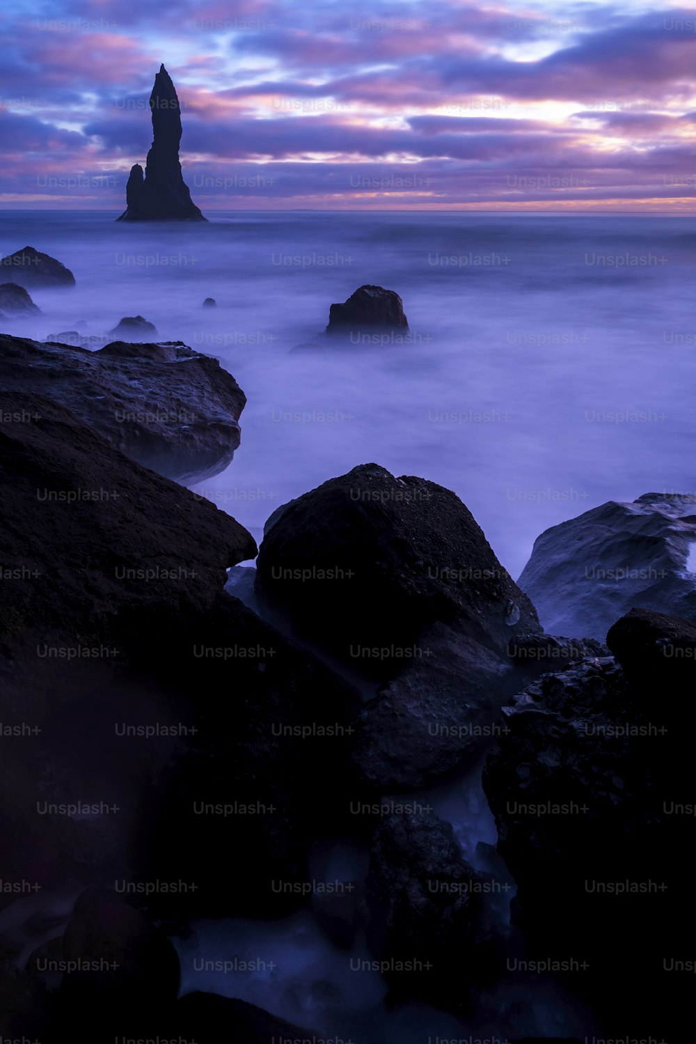 a long exposure photo of the ocean with rocks in the foreground