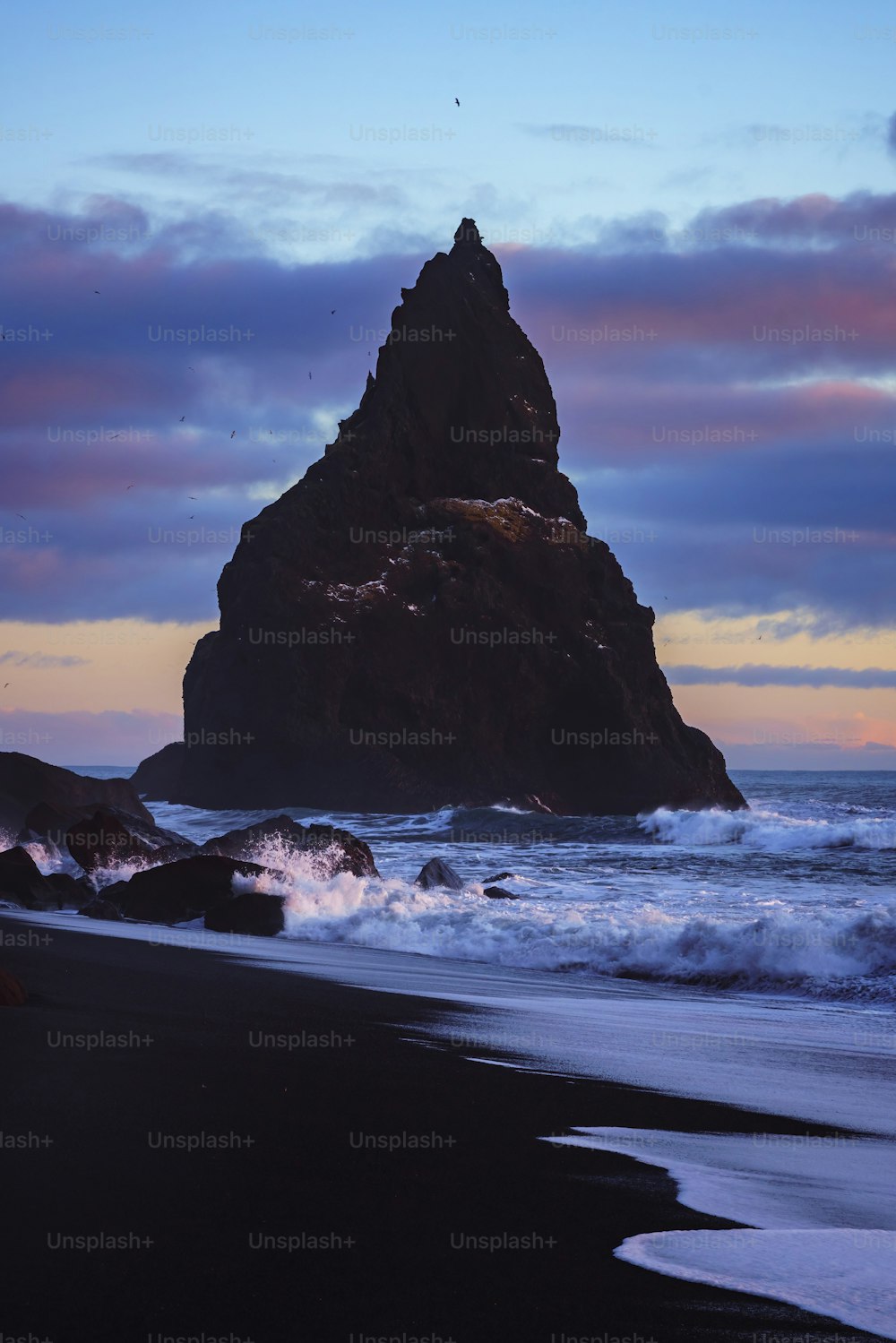 un gros rocher assis au sommet d’une plage au bord de l’océan