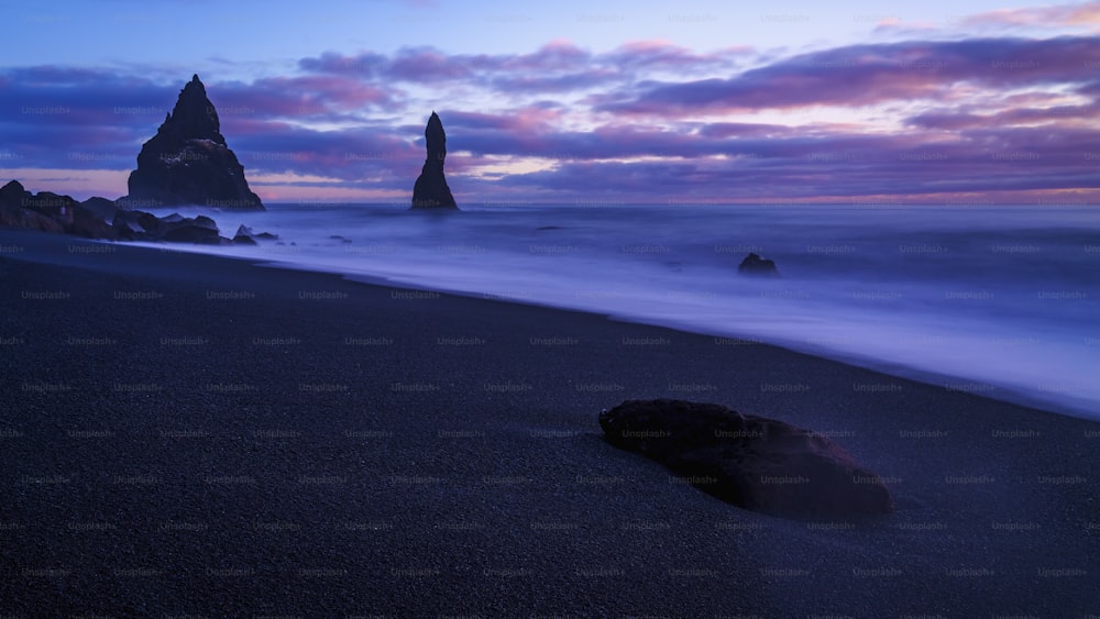 a beach with a rock in the foreground and a mountain in the background