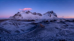 a snowy mountain range with a pink cloud in the sky