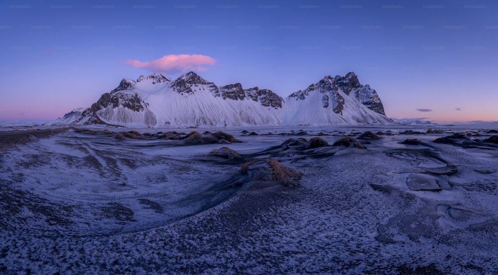 a snowy mountain range with a pink cloud in the sky