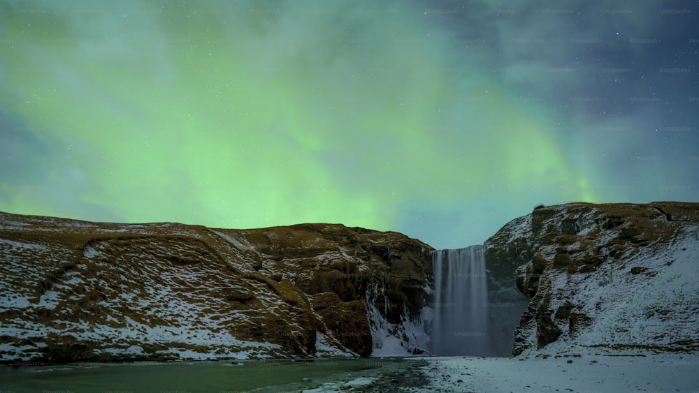 a waterfall with a green light in the sky
